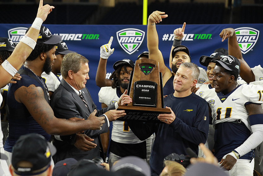 UToledo representatives holding the Reese Trophy, surrounded by cheering UToledo football players