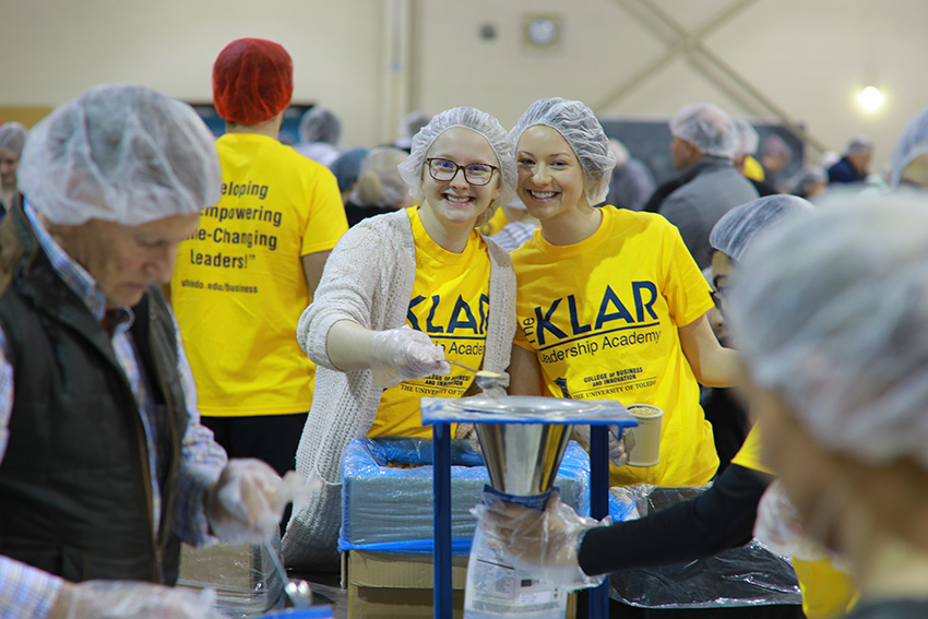 Two volunteers smiling while they pack meals together.