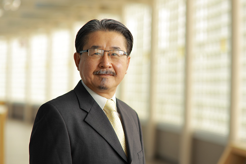 Dong Shik Kim, Ph.D., standing in a sun-lit hallway, wearing a business suit