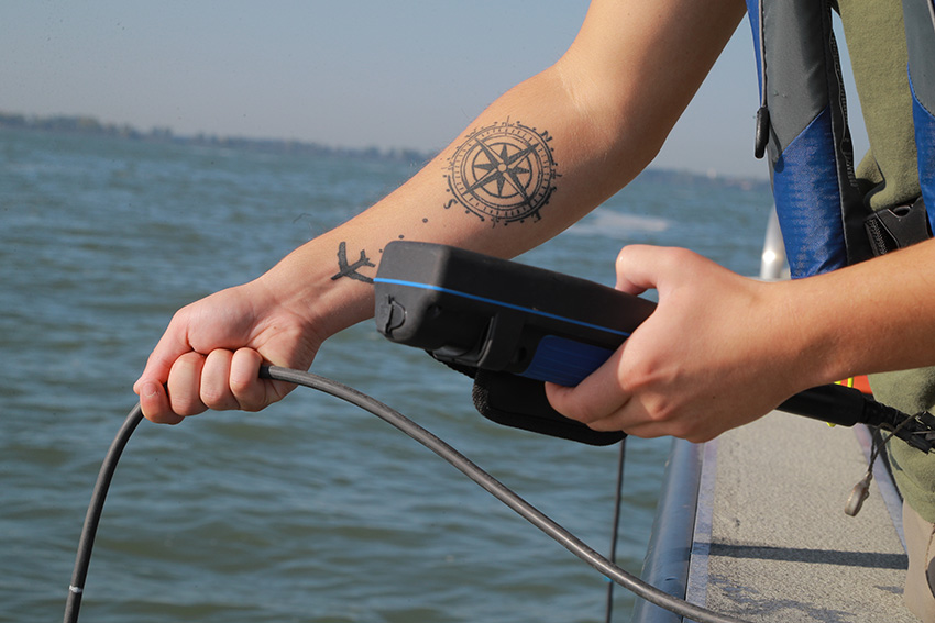 A pair of hands holding a measuring device from a boat above Lake Erie