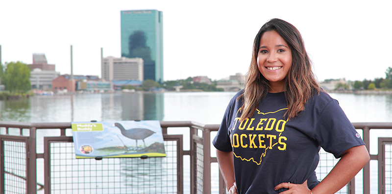 young woman in a Rockets t shirt posing by the Maumee River in downtown Toledo