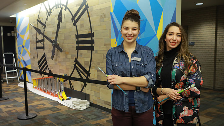 Rose Mansel-Pleydell and Tara Yarzand with clock mural in Carlson Library.