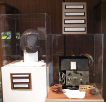 Pedestal exhibits showing a mask, women's undergarments, an ECT machine, leather straps, and medication brochures.