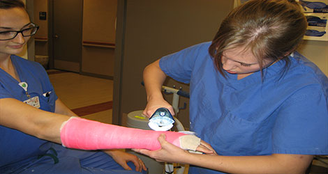 Resident working on removing a cast from the arm of a young woman