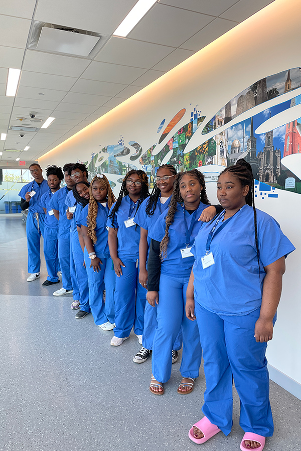 Students in blue scrubs stand in a hallway in the simulation center