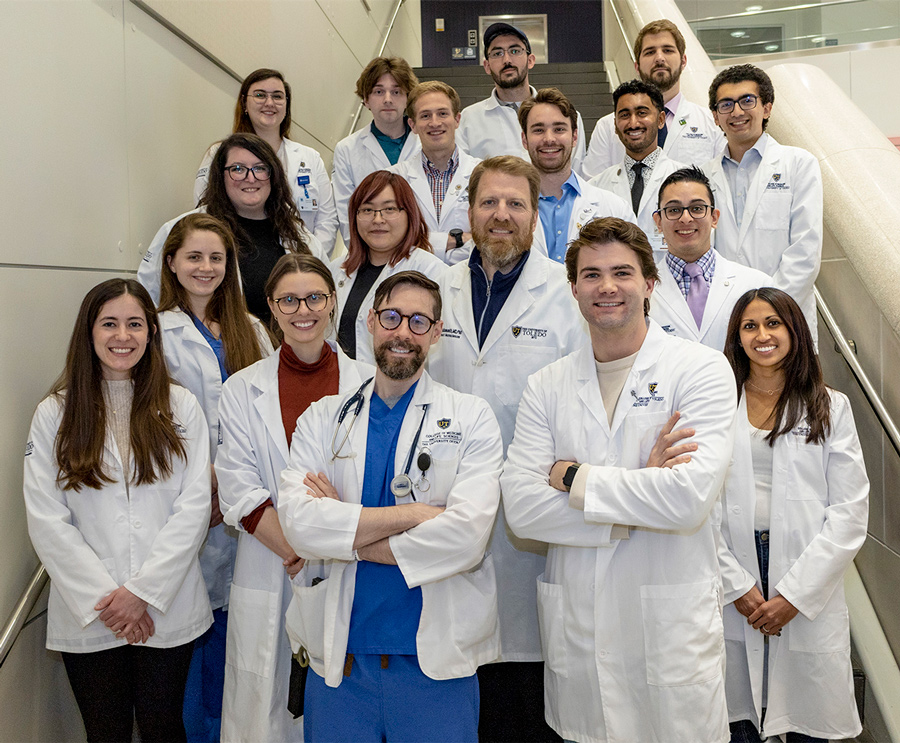 A group photo of M.D./Ph.D. students on a staircase in white coats.