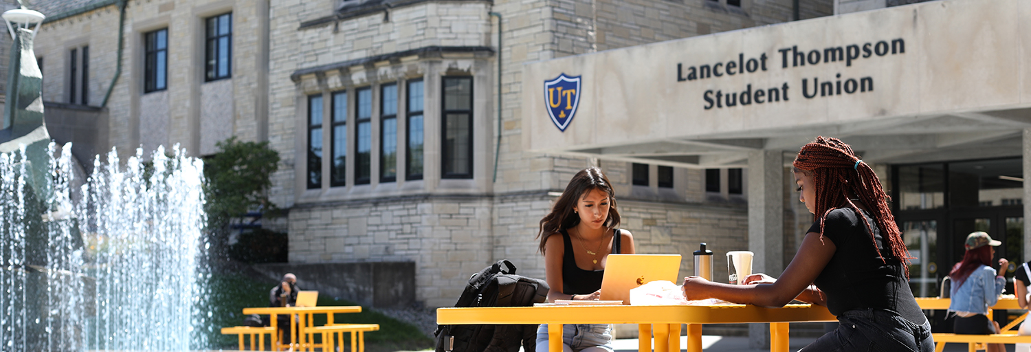 student sitting outside the Lancelot Thompson Student Union near the fountain