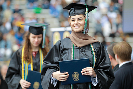 A young woman walks across stage after receiving her diploma at commencement