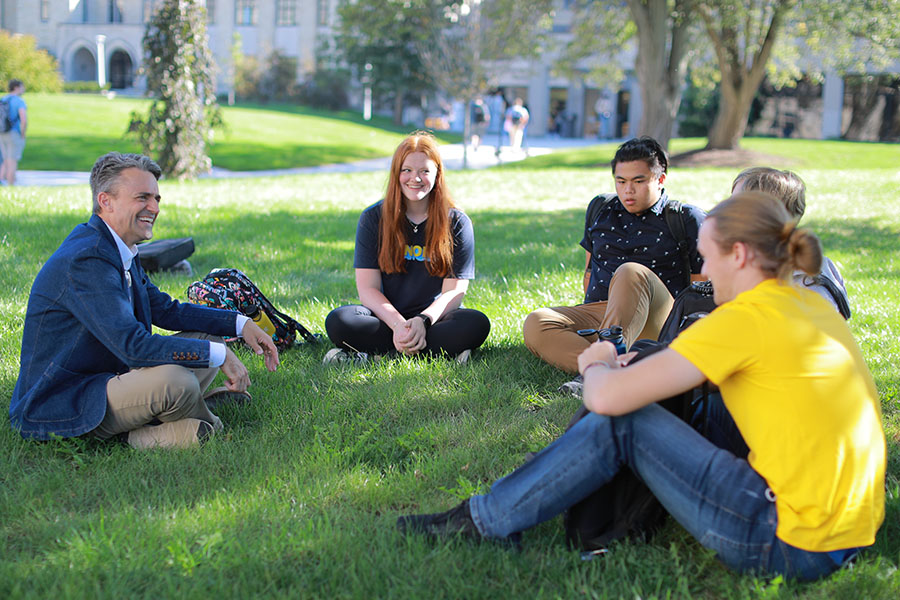 professor sitting on the grass outside with four students