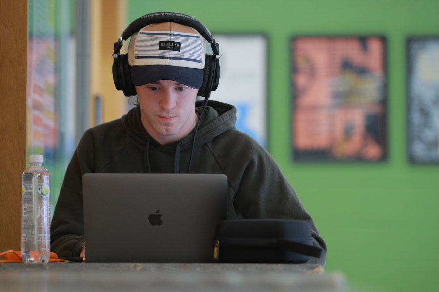 male online student in baseball cap and headphones in front of his laptop