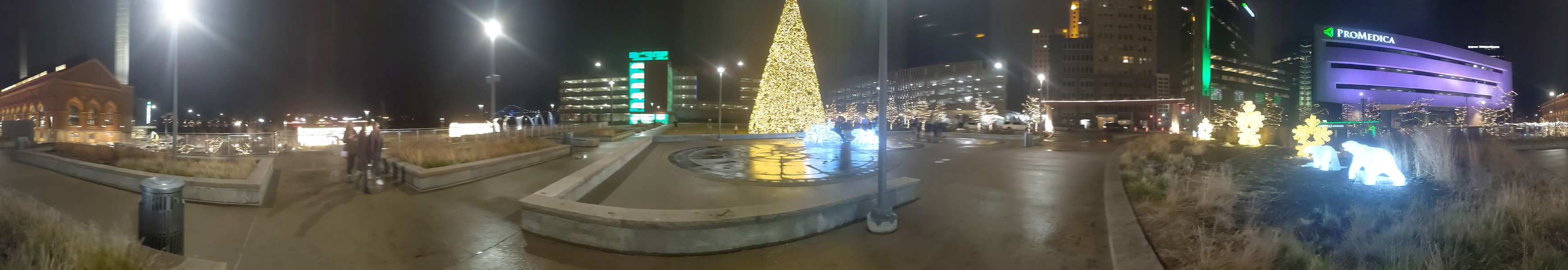 A panoramic night shot of downtown Toledo with a lit Christmas tree in the center.