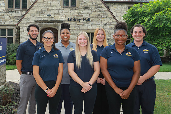 A diverse group of admission counselors standing together on UToledo's campus, smiling at the camera