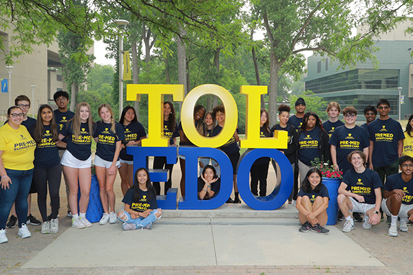 A large group gathered around a blue and gold statue that spells out TOL-EDO
