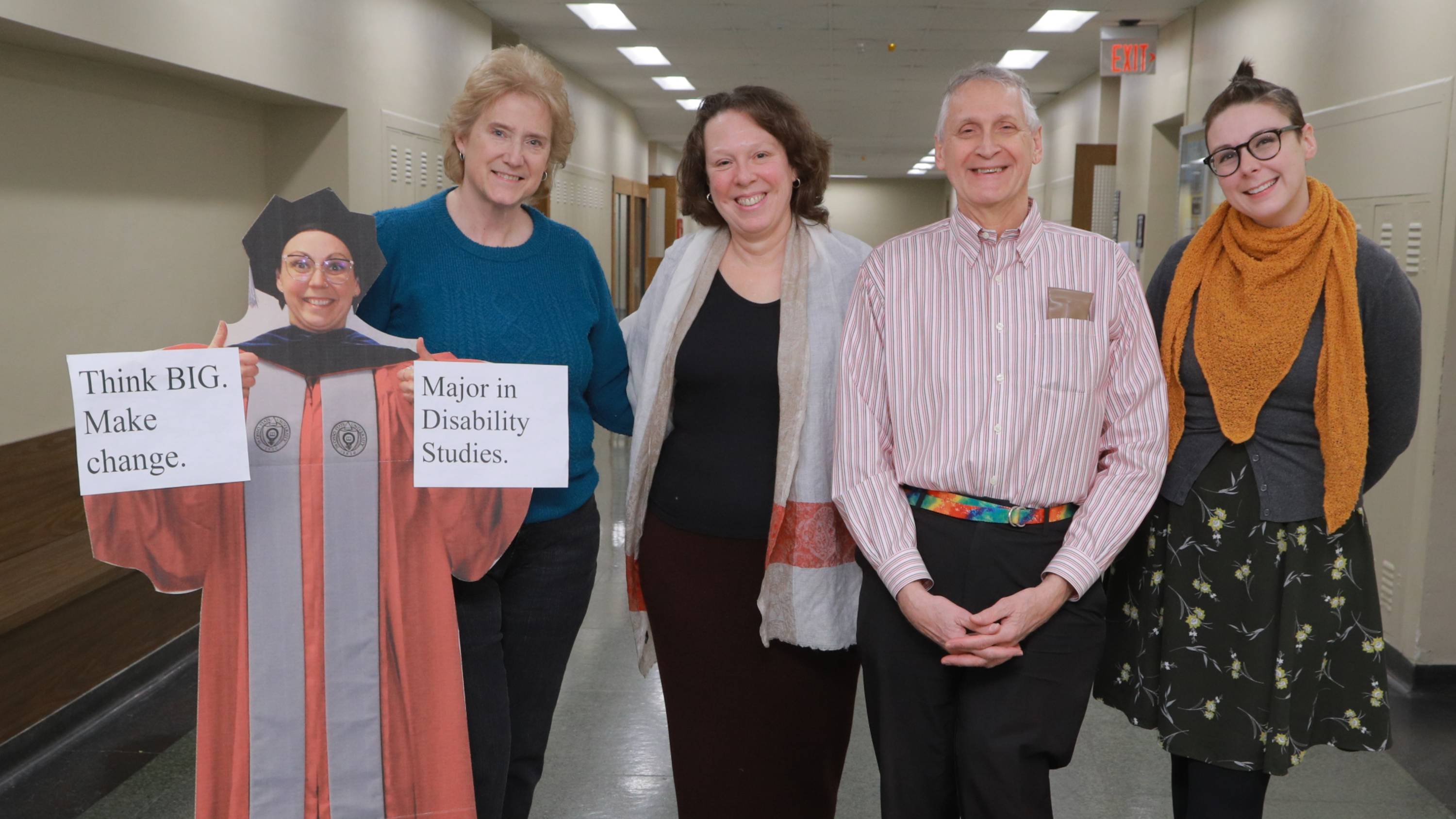 Disability Studies office administrator Linda Curtis standing with professors Kim Nielsen, Jim Ferris, and Becca Monteleone, smiling in a hallway. They are next to a cardboard cutout of professor Ally Day with signs that say "Think Big, Make Change. Major in Disability Studies Disability Studies office administrator Linda Curtis standing with professors Kim Nielsen, Jim Ferris, and Becca Monteleone, smiling in a hallway. They are next to a cardboard cutout of professor Ally Day with signs that say "Think Big, Make Change. Major in Disability Studies