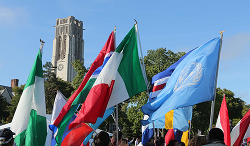 people on UToledo main campus carrying flags from many nations with UToledo tower in background