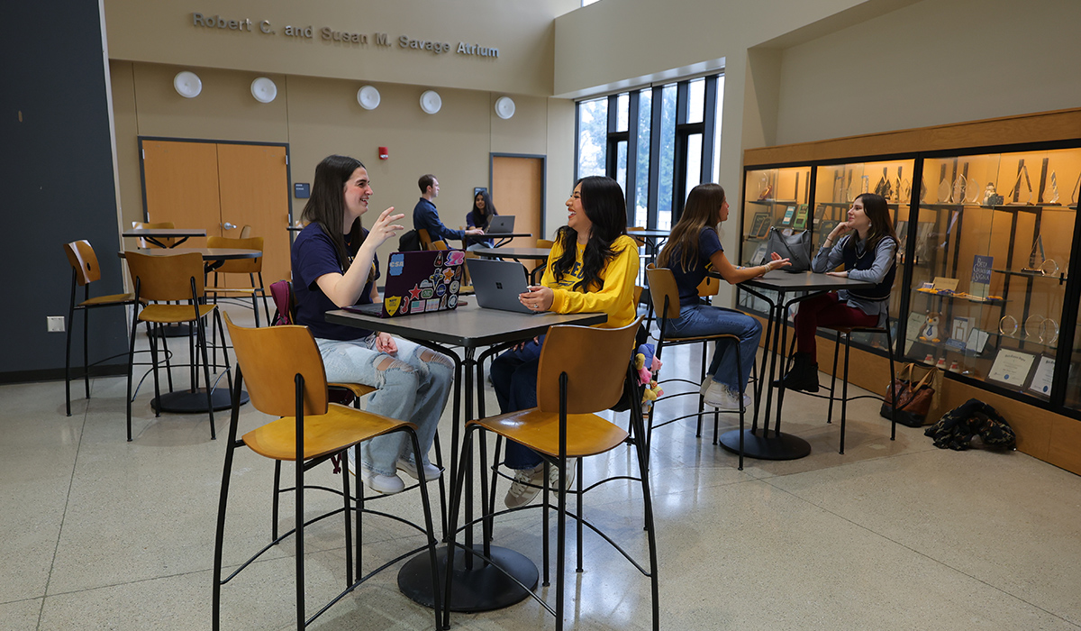 College of Business students sitting at tables in the savage and associates complex, students are talking to each other and working on their laptops