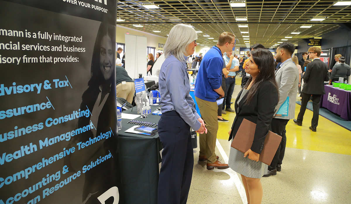 A female college of business student at the business careers fair talking with an employer. 