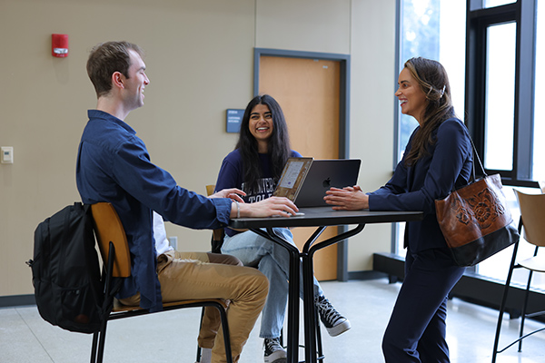 3 college of business students sitting at a table taking and working on their computers