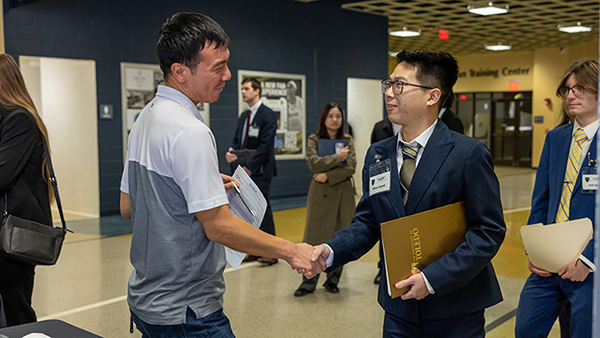 a business student shanking hands and greeting an emloyer at the college of business career fair