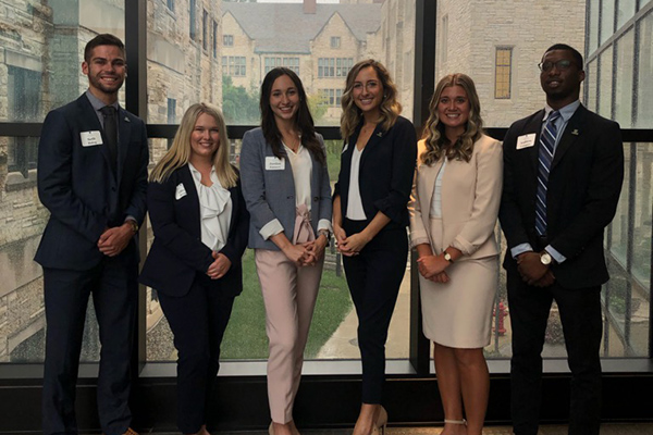professional sales students taking a group photo infront a glass window with academic bulidngs and University Hall in the background