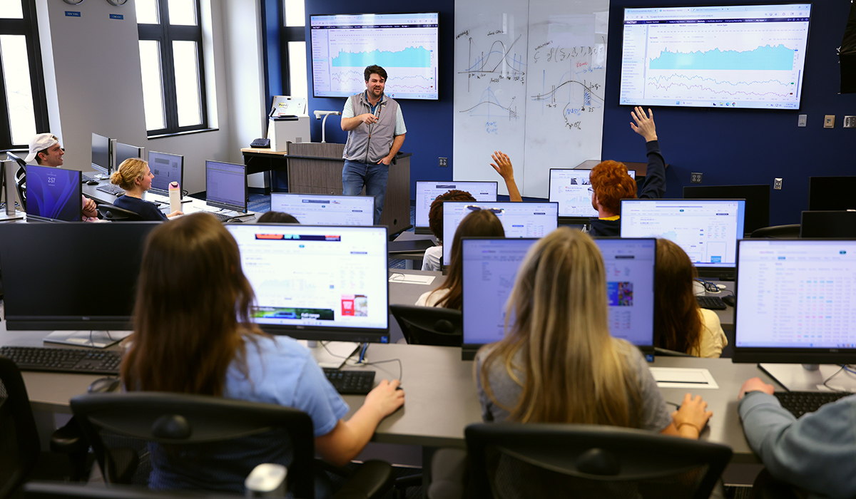 Neff college of business Associate Professor Collin Gilstrap teaching a classroom full of business students in the neff trading room