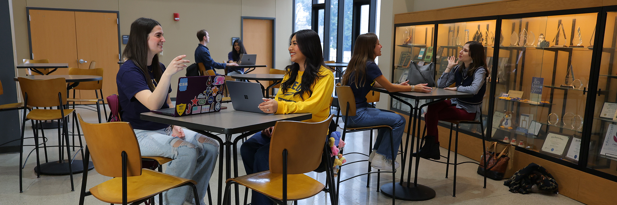 College of Business students sitting at tables in the savage and associates complex, students are talking to each other and working on their laptops