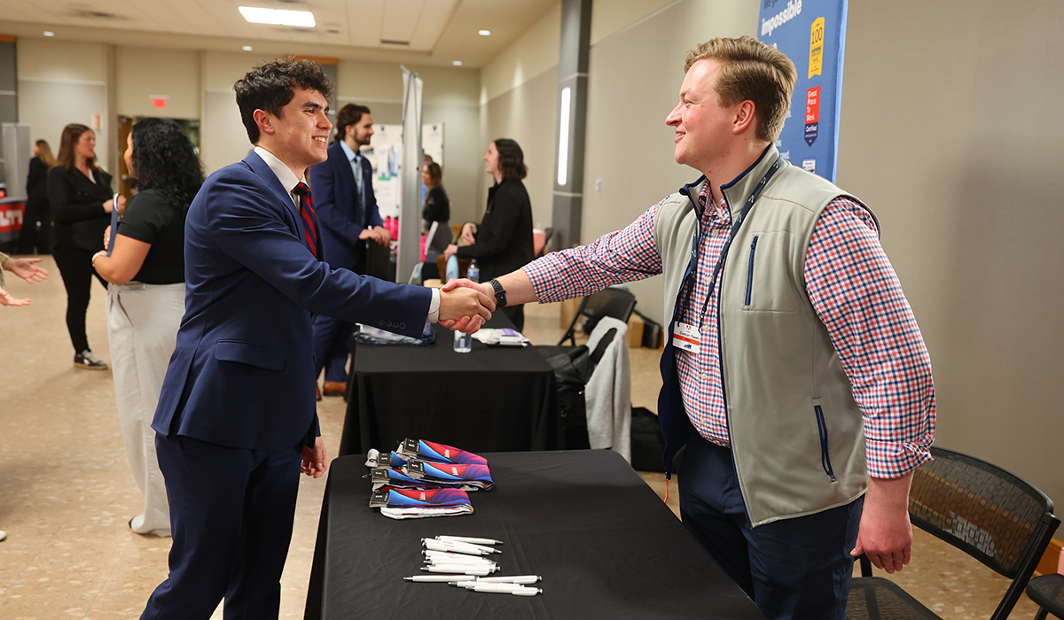 Business student dressed in business professional attire meeting and shaking hands with an employer at a business job fair