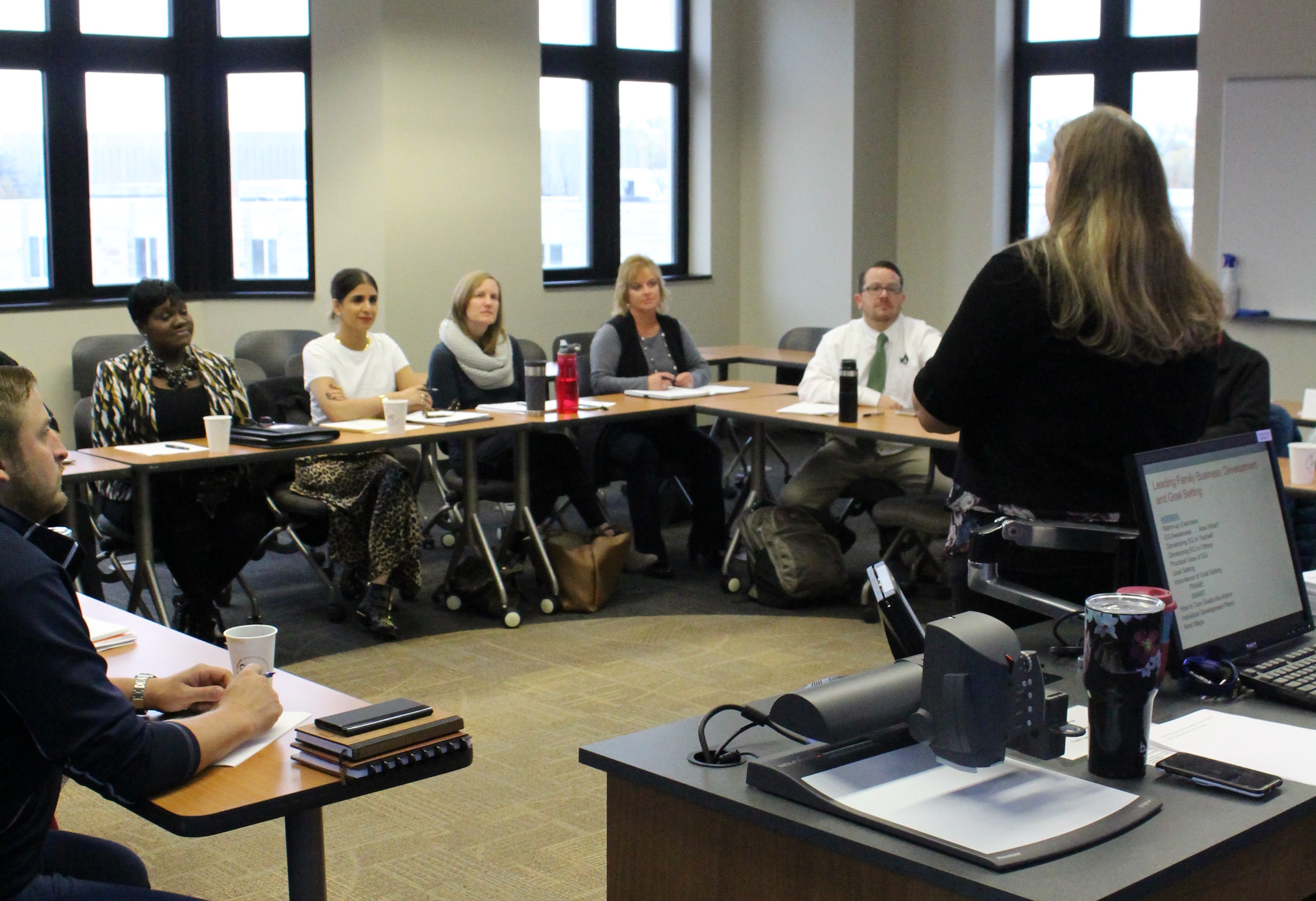 Woman facing a class teaching 3 women and 1 man who are sitting at desks.