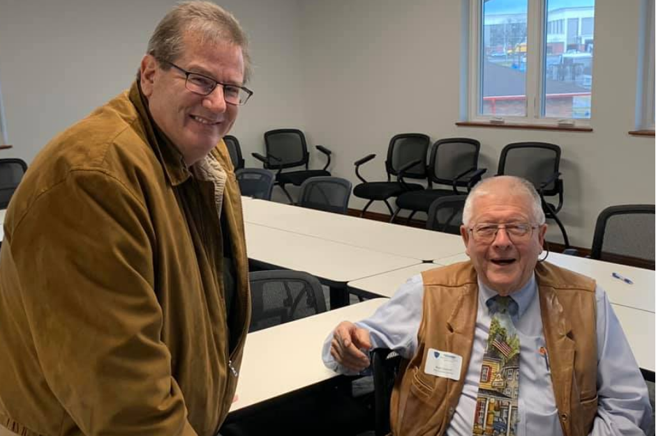 Two center members posing for a picture. One man is standing up and the other is sitting down.