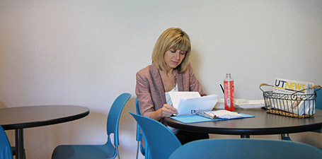 woman sitting at a table with a water bottle reading a piece of paper