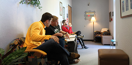 three men sitting on lounge chairs talking and pointing at their notebooks