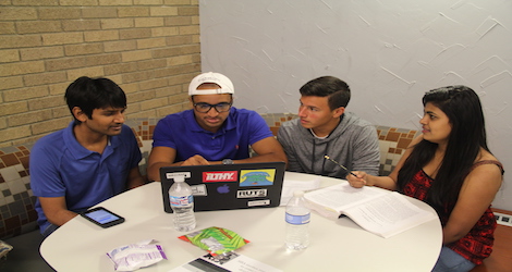 4 individuals sitting around a laptop computer staring at the screen