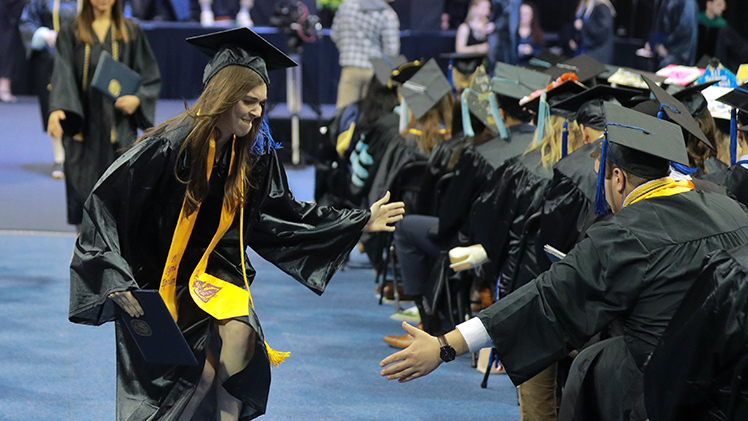 afternoon commencement ceremony - student giving a high five after recieving diploma