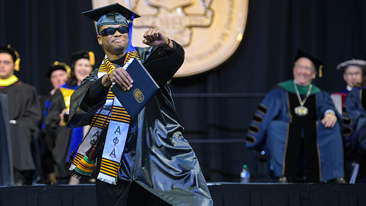 afternoon commencement ceremony - student giving a high five after recieving diploma