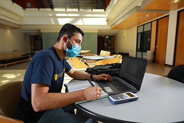a male student wears a mask and works on his computer