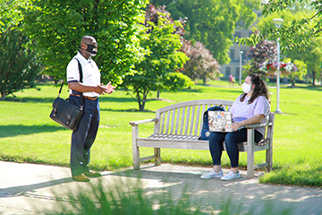 masked man talks to masked woman on a bench