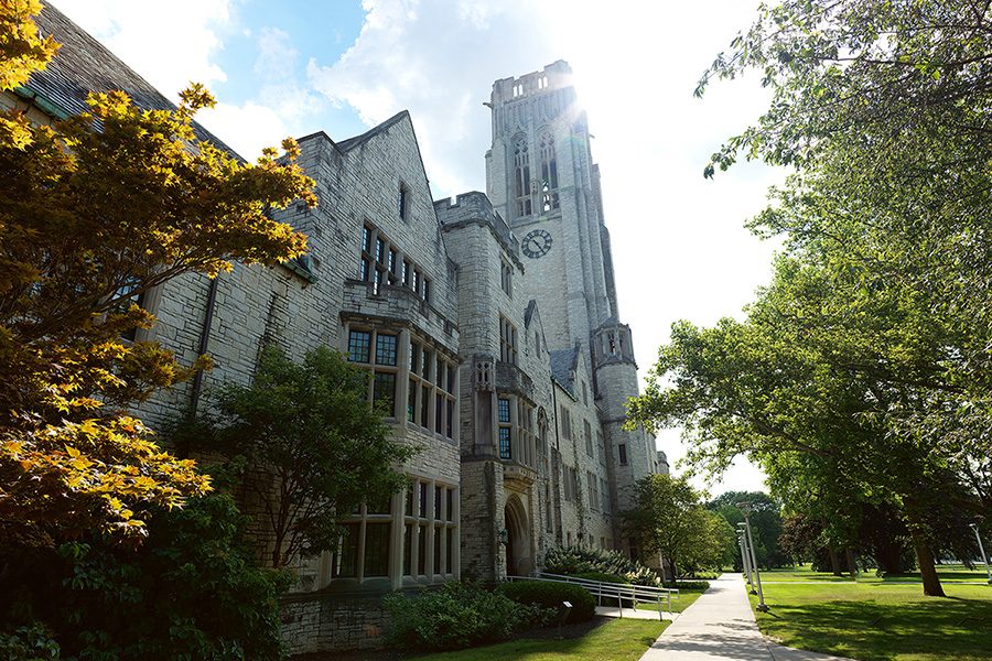 university hall and walkway, stone building with clock tower surrounded by green grass and trees