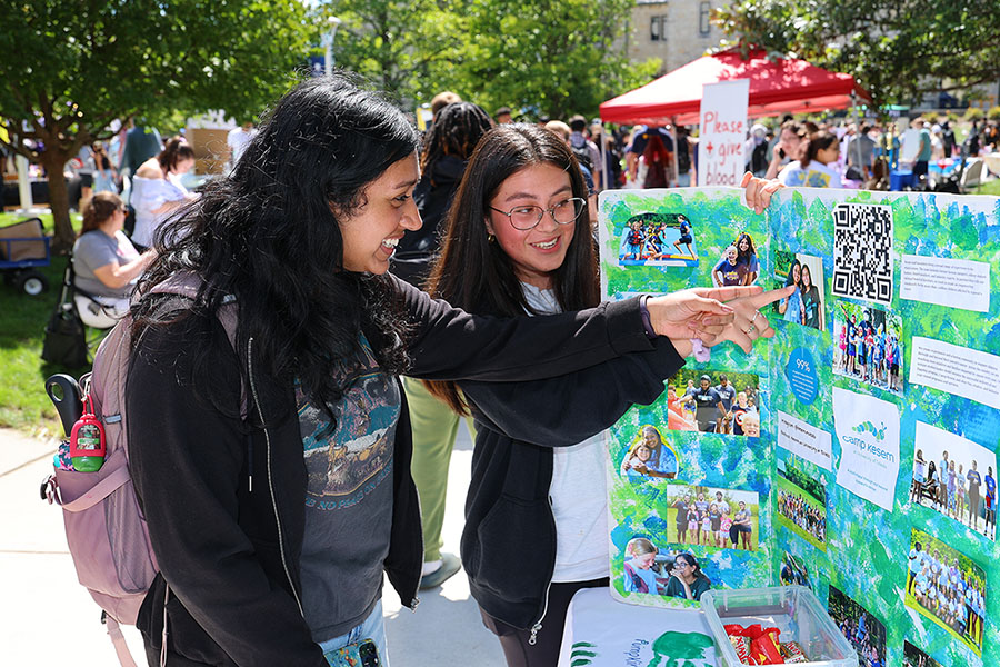 two girls pointing at a poster and smiling at the campus involvement fair