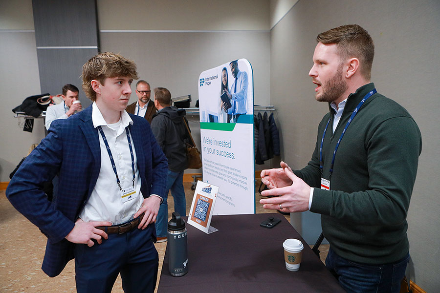two guys discussing business in front of a booth at a sales event