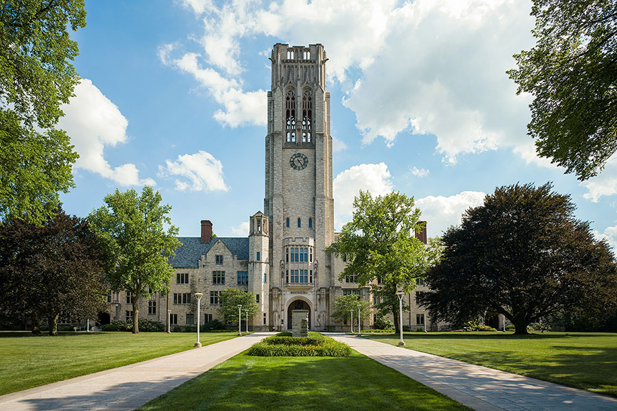university hall, stone building with clock tower in summer surrounded by green grass and trees