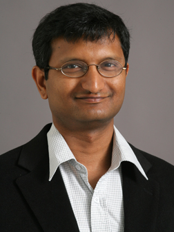 smiling dark haired man in suit and tie with glasses