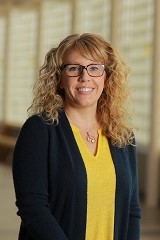 smiling blond woman with glasses in blue and gold clothing