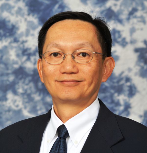 smiling dark haired man with glasses in dark suit and tie
