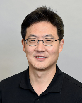 headshot of smiling dark haired man with glasses in navyblue shirt