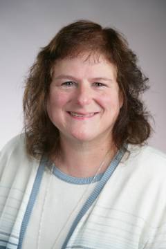 smiling, brown-haired woman in white and blue sweater