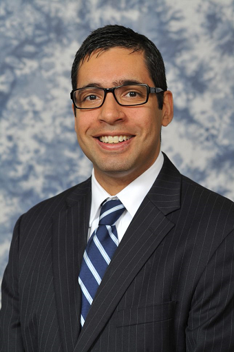 smiling dark haired man with glasses in dark suit and tie