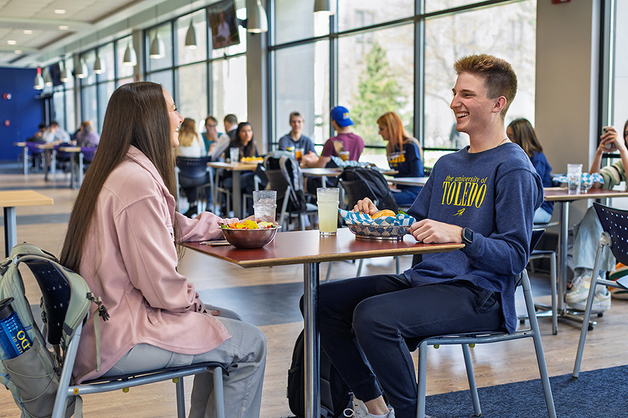 two students sitting at a table in the dining hall eating lunch and talking