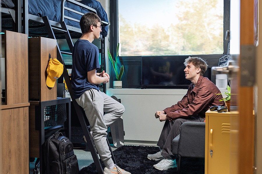 two students in a residence hall room talking and smiling