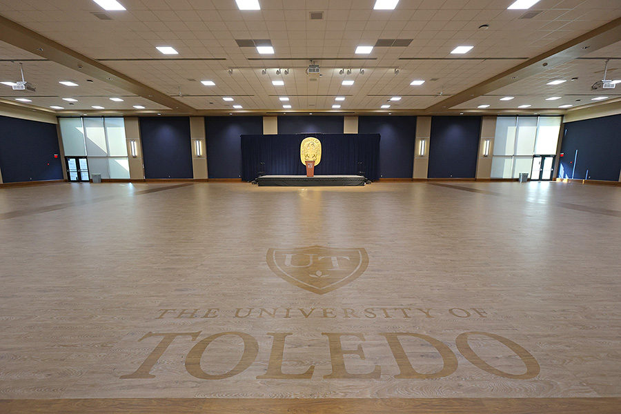 empty auditorium with stage gold university seal, and “The University of Toledo” logo on wood floor