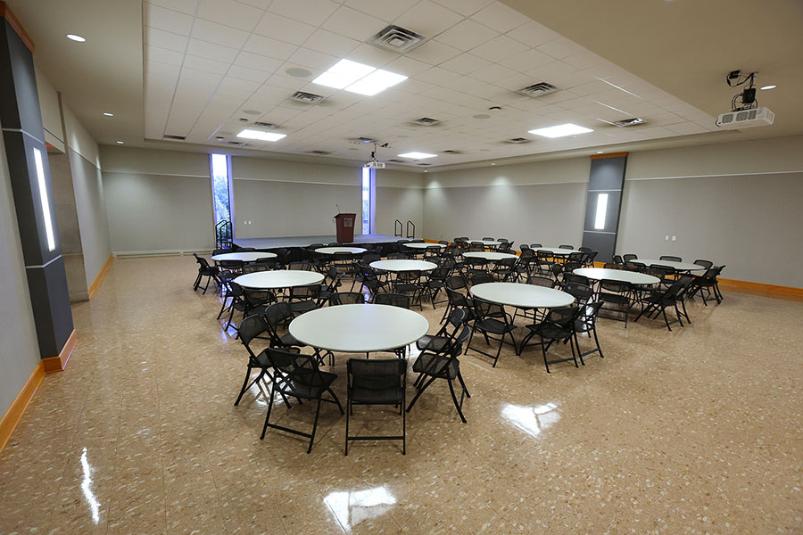 Large multipurpose room with round tables and black folding chairs.